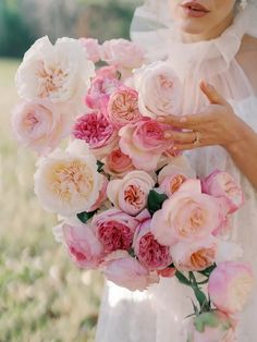 a bride holding a bouquet of pink and white flowers in her hands, with grass behind her