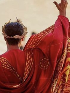 a man dressed in red and gold holding his hands up to the sky while wearing a crown