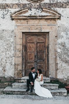 a bride and groom sitting on steps in front of an old building with wooden doors