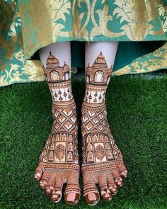 the legs and feet of a woman with henna tattoos on them, standing in grass