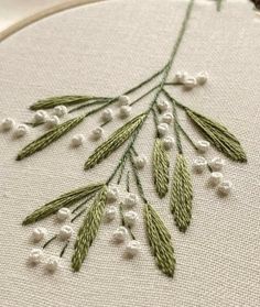 a close up of a embroidery on a hoop with white beads and green leaves in it