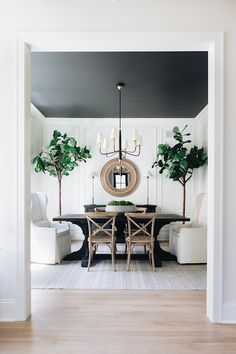 the dining room is decorated in black and white with greenery on the table, along with two large potted trees