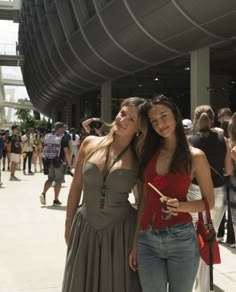 two young women standing next to each other in front of a building with lots of people