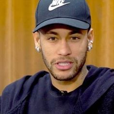 a man wearing a nike cap and earring sitting in front of a wooden wall