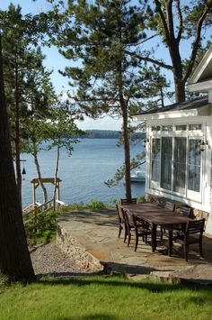 a table and chairs are outside by the water's edge with trees around it