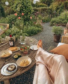 a woman sitting at a table with food and wine in front of her, looking out onto the garden