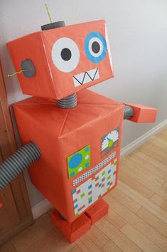 an orange robot made out of cardboard sitting on top of a hard wood floor next to a door