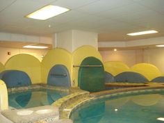 an indoor swimming pool with yellow and blue walls, water features in the center area