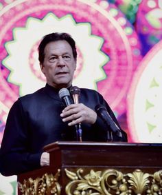 a man standing at a podium holding a microphone in front of a colorful wallpaper