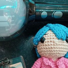 a crocheted doll sitting on top of a table next to a cell phone