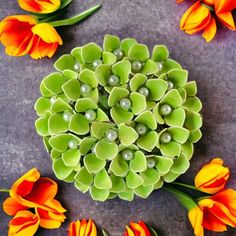 an arrangement of orange and yellow tulips with pearls in the center on a gray surface