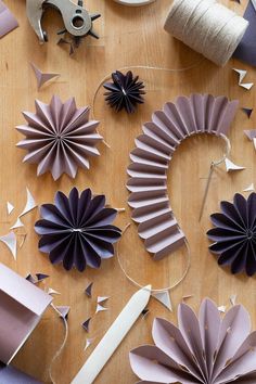 several different types of paper flowers on a wooden table with scissors and thread spools