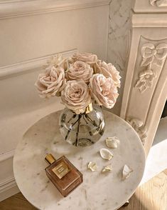 a marble table with flowers in a vase and a perfume bottle on the side next to it