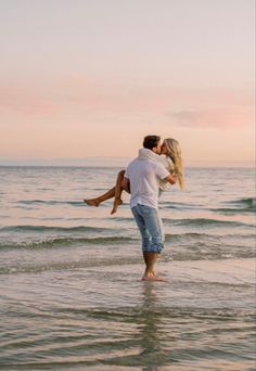 a man and woman kissing in the ocean with their arms around each other as they walk into the water