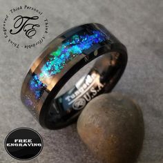 a black ring with blue and green fire opal inlayed to it, sitting on top of a rock