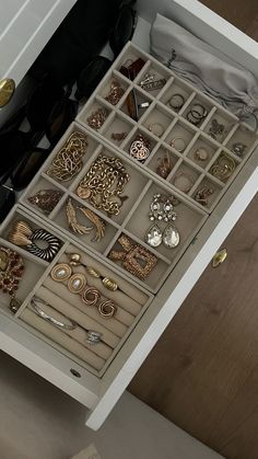 a drawer filled with lots of jewelry on top of a wooden floor next to a white cabinet