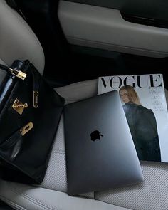 an apple laptop sitting on top of a car seat next to a handbag and magazine