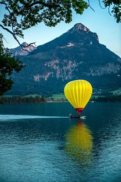 a large yellow hot air balloon floating on top of a lake next to a mountain