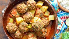 meatballs and potatoes are in a brown bowl on a colorful cloth with a spoon