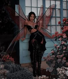 a woman in a black dress and fairy wings posing for a photo with flowers behind her