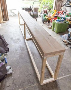 a wooden bench sitting in a garage next to a bag and other items on the floor