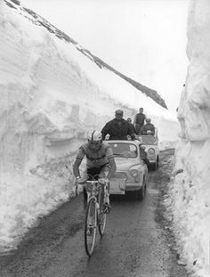 a man riding a bike down a snow covered road next to a car and truck