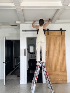 a woman is standing on a ladder and painting the ceiling