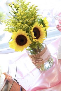 a vase filled with sunflowers sitting on top of a pink table cloth next to a cake