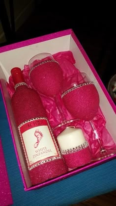 a pink box with four wine glasses and a bottle in it on top of a table