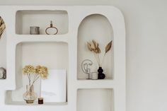 white shelves with vases, flowers and other items on them are arranged in the shape of an arch