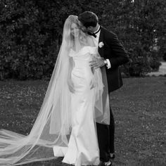 a bride and groom standing in front of some bushes with their veil blowing in the wind