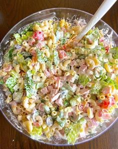 a bowl filled with pasta salad on top of a wooden table next to a plastic spoon