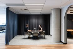 two people sitting at a round table in an office with black drapes on the walls