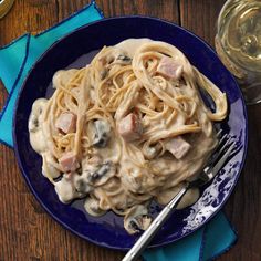 a blue plate topped with pasta and meat covered in mushroom sauce next to a glass of wine