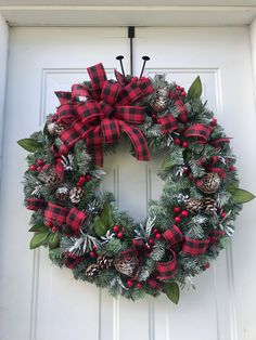 a christmas wreath hanging on the front door with pine cones, holly berries and bells