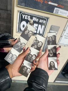 two hands holding up several photos of people in front of a vending machine that says yes, we are open