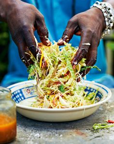 two hands grabbing shredded vegetables from a bowl on a table with orange juice in the background