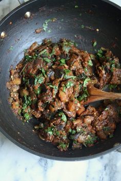 meat and vegetables cooking in a skillet with a wooden spoon