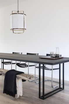 a dining room table with chairs and a bench in front of it, next to a white wall