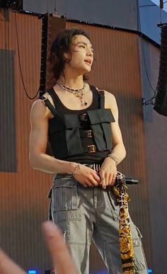 a woman standing on top of a stage holding a microphone in her right hand and wearing an animal print scarf around her neck