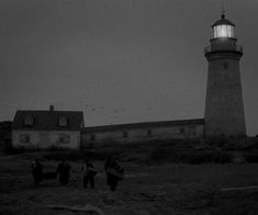 three people carrying surfboards in front of a lighthouse