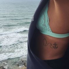 a woman with a small anchor tattoo on her lower side ribcage, standing next to the ocean