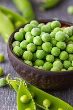 peas are in a bowl on a table next to pea pods and green beans,