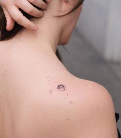 the back of a woman's shoulder with small dots on it and an object behind her