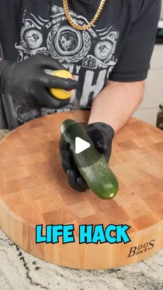 a person wearing black gloves and holding a pickle on top of a wooden cutting board