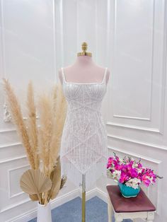 a mannequin is next to a vase with flowers and feathers on display in a white room