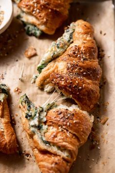 some croissants with spinach and cheese on them are sitting on a piece of parchment paper