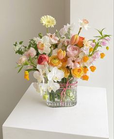 a vase filled with lots of different colored flowers on top of a white table next to a wall