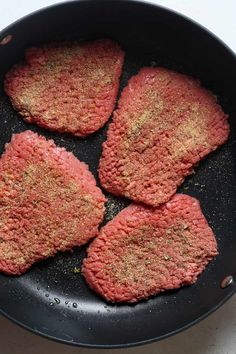 four hamburger patties in a frying pan on the stove top, ready to be cooked