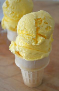 three scoops of yellow ice cream sitting on top of a wooden table next to each other